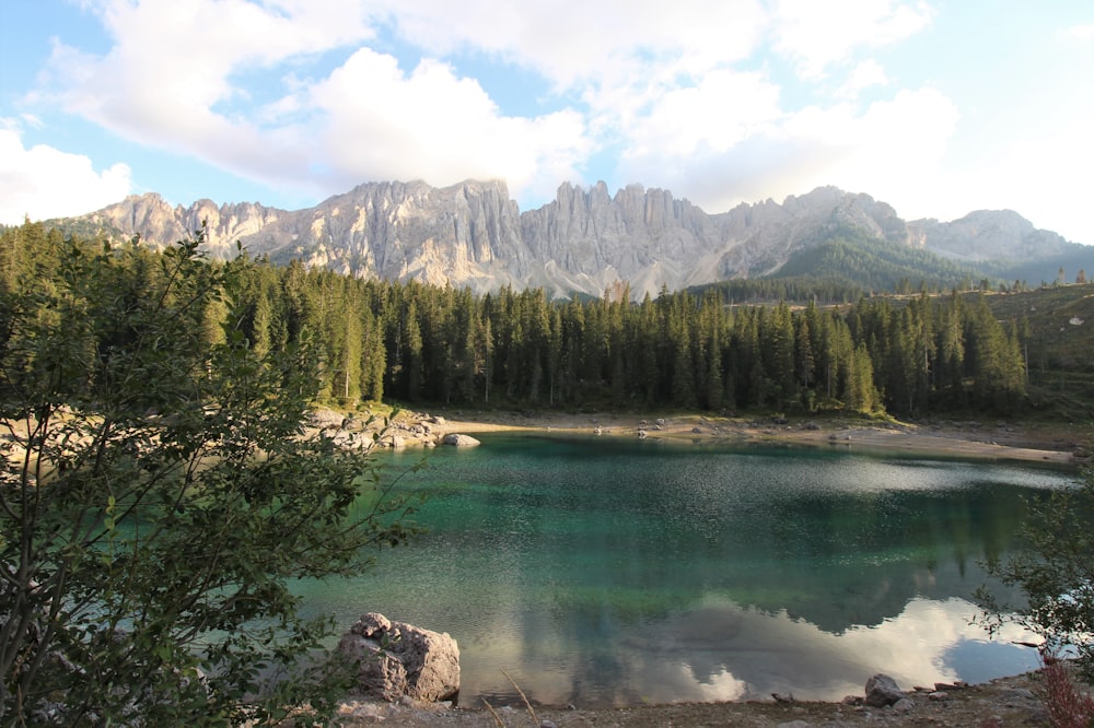 a lake surrounded by trees and mountains under a cloudy sky