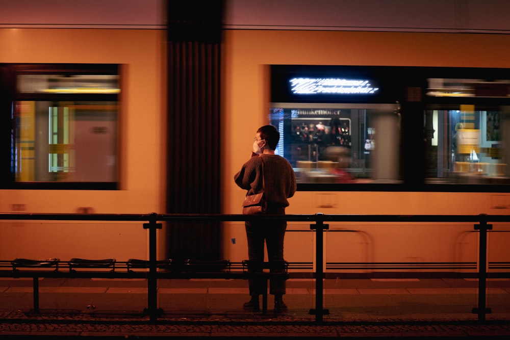 a man standing on a train platform while talking on a cell phone