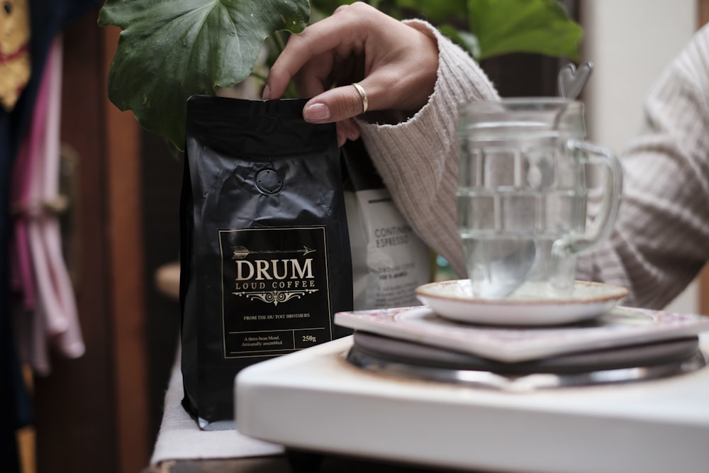 a person holding a bag of coffee next to a plant