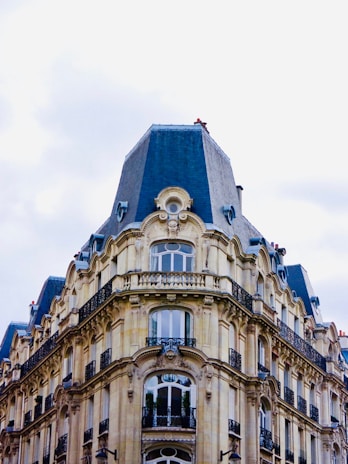An ornate, historic building with a mansard roof, featuring detailed stonework and wrought iron balconies. The architecture exemplifies a classic, European style with multiple arched windows and elegant facades.