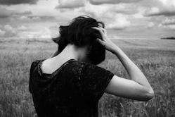 a woman standing in a field of tall grass, frustrated with trauma patterns before hypnotherapy