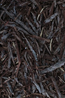 A collection of overlapping pieces of bark, with various shades of brown and gray. The texture is rough and natural, resembling a typical organic mulch used in gardening.