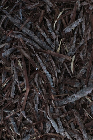 A collection of overlapping pieces of bark, with various shades of brown and gray. The texture is rough and natural, resembling a typical organic mulch used in gardening.