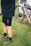 A person wearing cycling attire, specifically black shorts and gray cycling shoes, is standing on grass next to a bicycle that is positioned against a white structure. The bicycle is equipped with bags, indicating it may be prepared for a long ride or cycling tour.