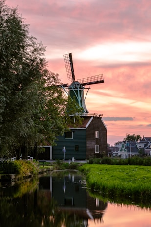 A traditional Dutch windmill standing tall against a sunset backdrop over green meadows.