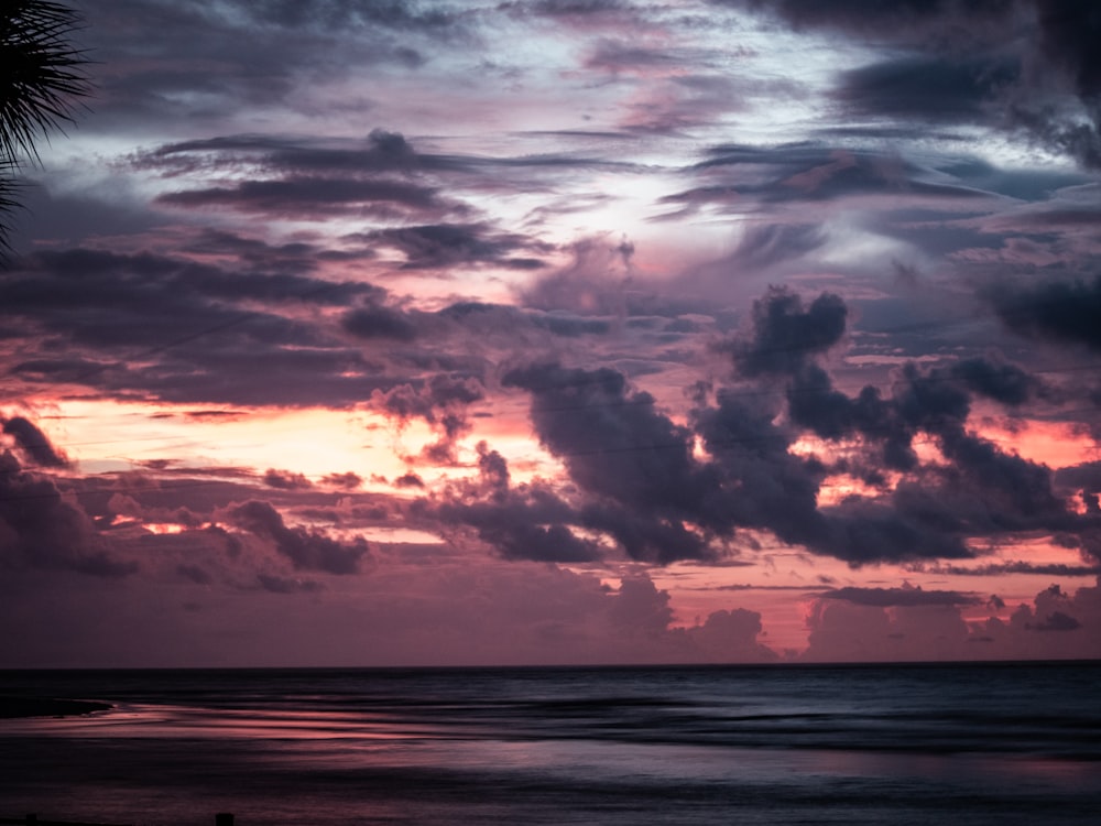 the sun is setting over the ocean with clouds in the sky