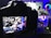 A digital camera is positioned to capture an image displayed on its screen. The screen shows a vivid and colorful scene featuring a pair of Nike sneakers, vibrant neon lights, and graphic elements in the background. The setup suggests a creative and modern product photography shoot.