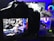 A digital camera is positioned to capture an image displayed on its screen. The screen shows a vivid and colorful scene featuring a pair of Nike sneakers, vibrant neon lights, and graphic elements in the background. The setup suggests a creative and modern product photography shoot.