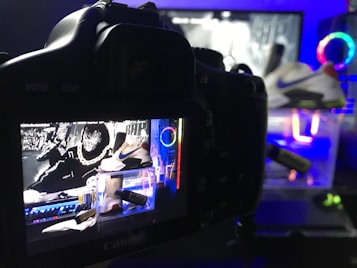 A digital camera is positioned to capture an image displayed on its screen. The screen shows a vivid and colorful scene featuring a pair of Nike sneakers, vibrant neon lights, and graphic elements in the background. The setup suggests a creative and modern product photography shoot.
