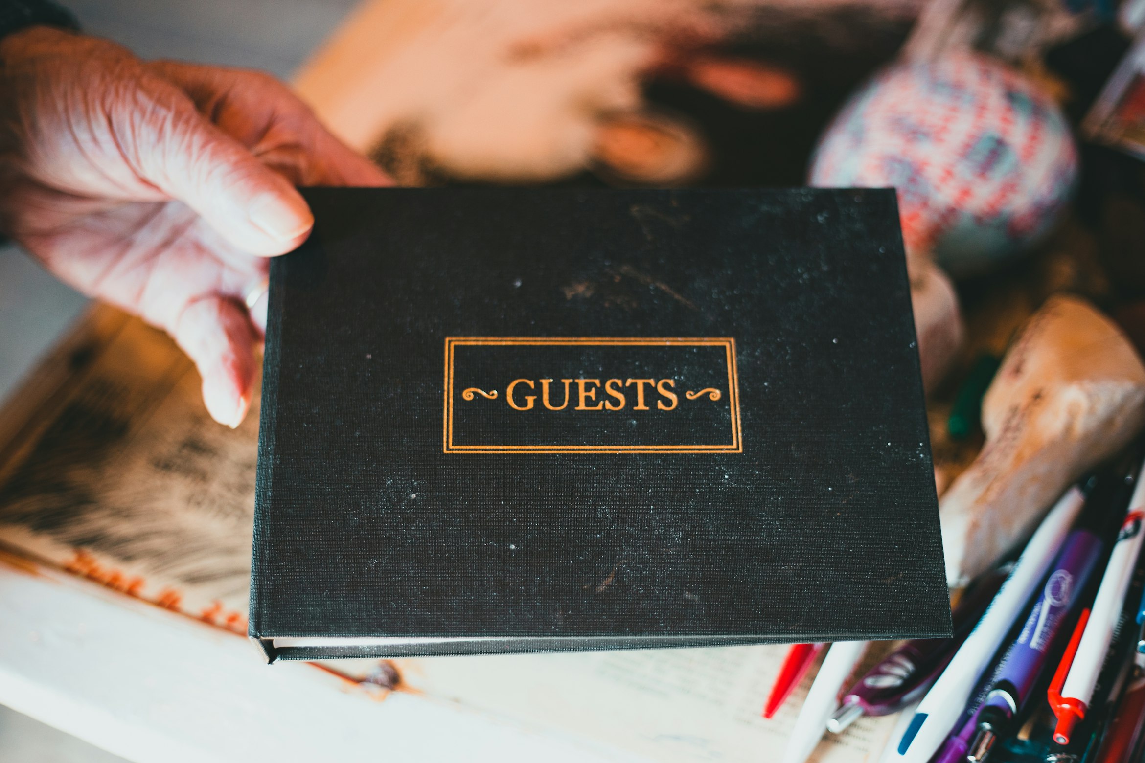 a human hand holding a black bound book with the word "Guests" printed in a gold color