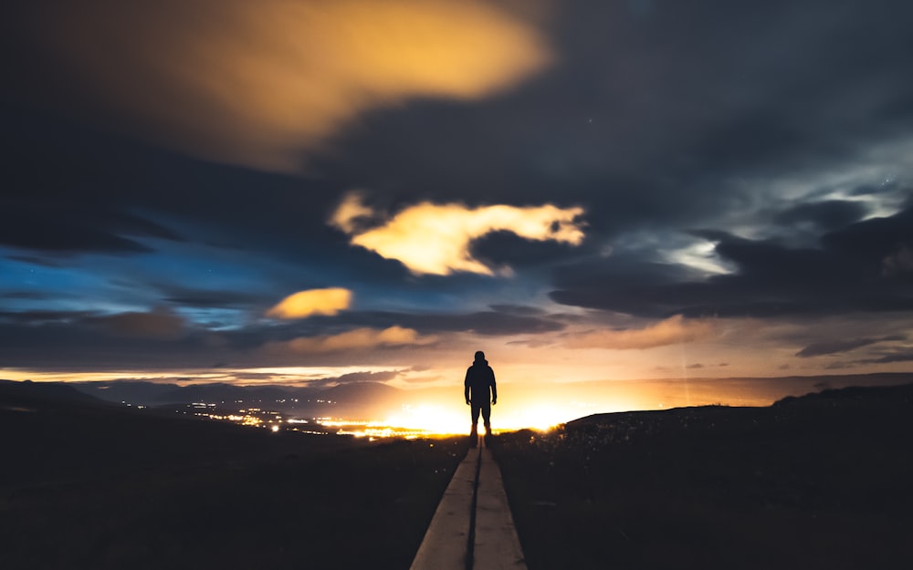 une personne debout sur une route au coucher du soleil