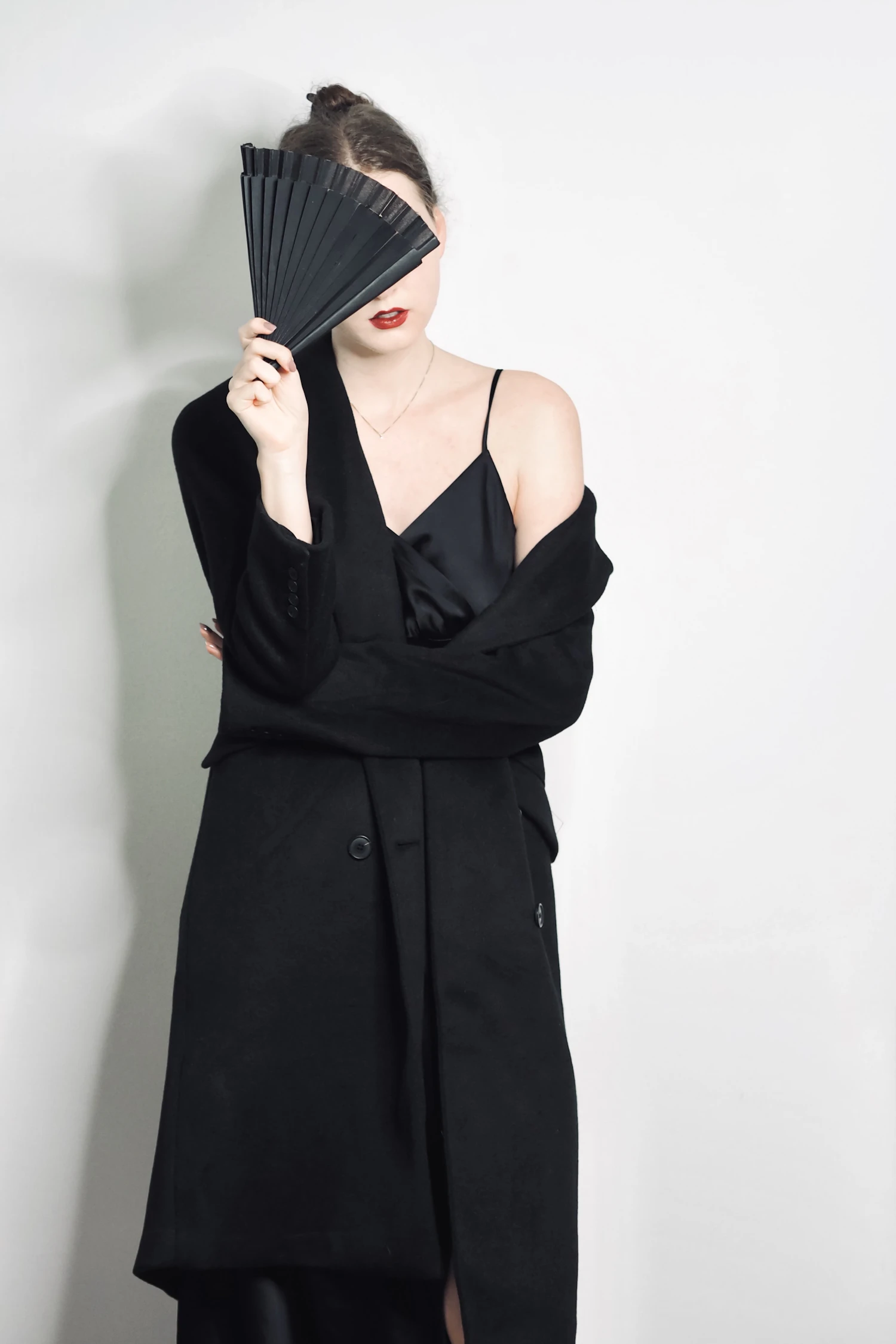 A long dark coat worn over a slip, the face half covered by a fan