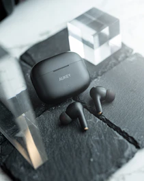 A sleek matte black wireless earbud set resting on a minimalist graphite desk with soft ambient lighting.