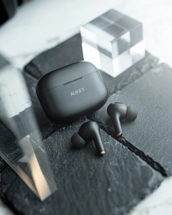 A sleek matte black wireless earbud set resting on a minimalist graphite desk with soft ambient lighting.