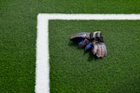 A pair of colorful goalkeeper gloves lies on a green soccer field near the white boundary line.