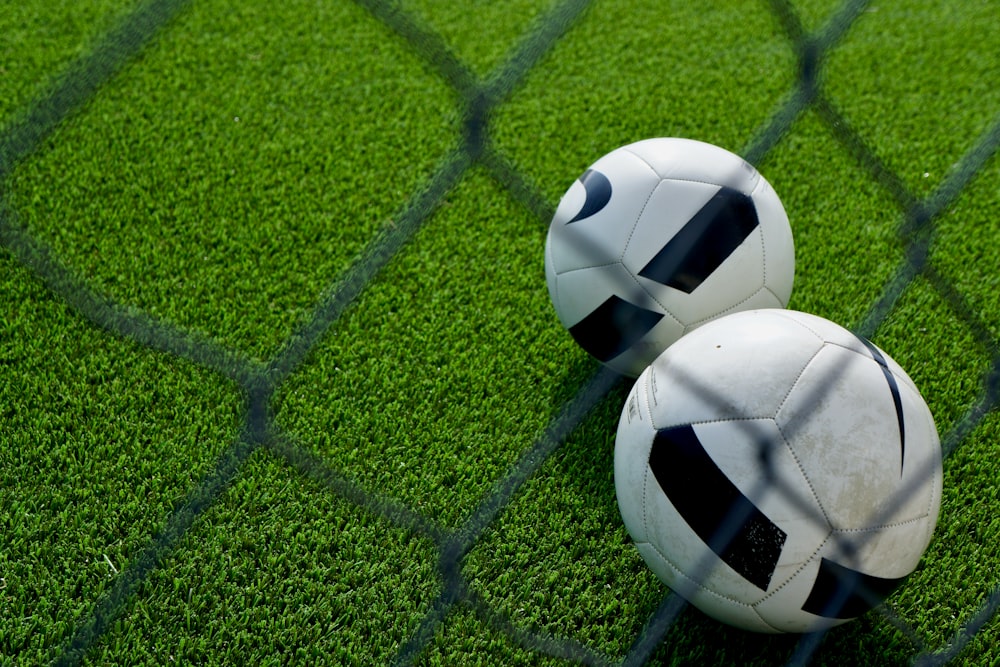 two soccer balls sitting on top of a green field