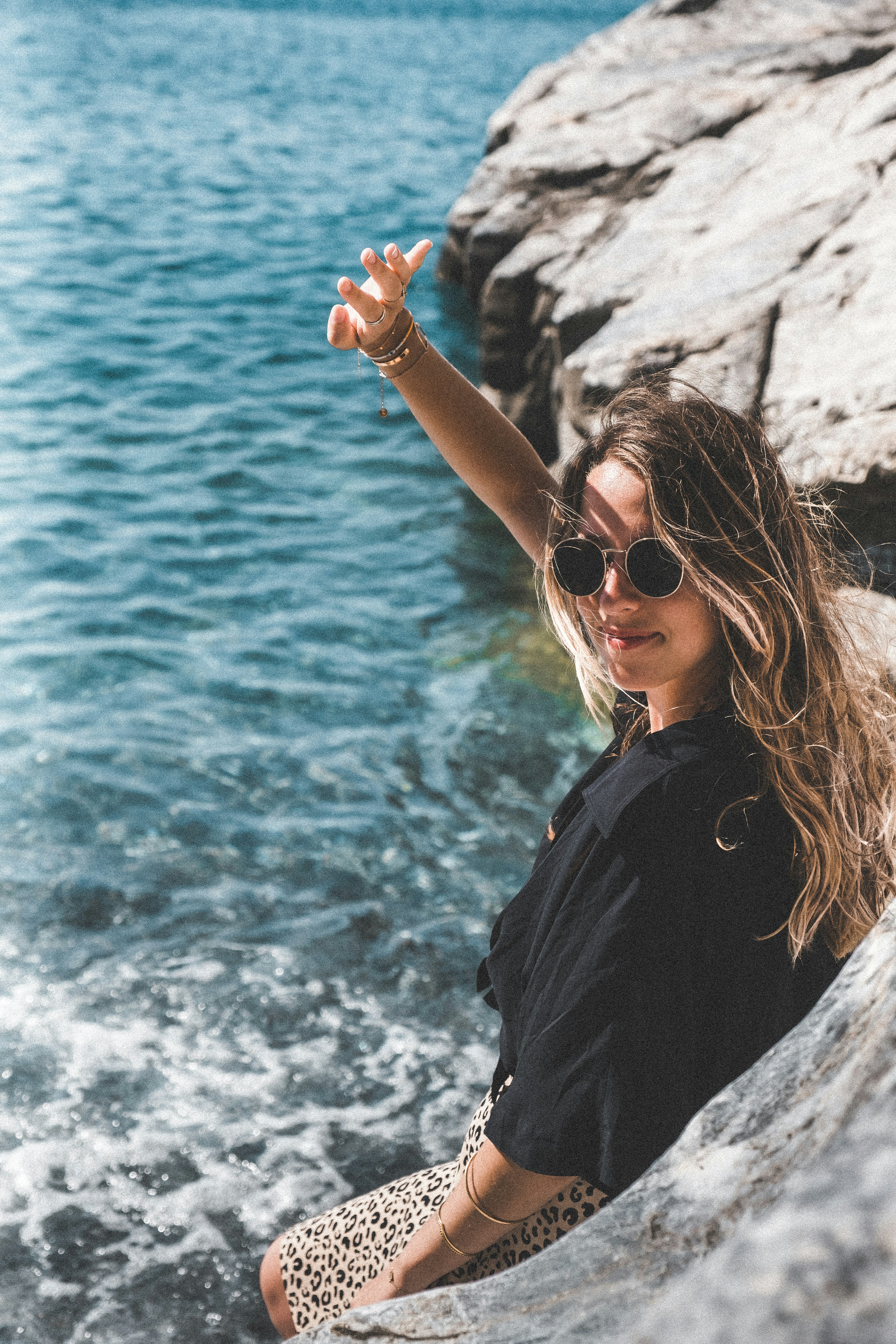 a woman sitting on top of a rock next to a body of water