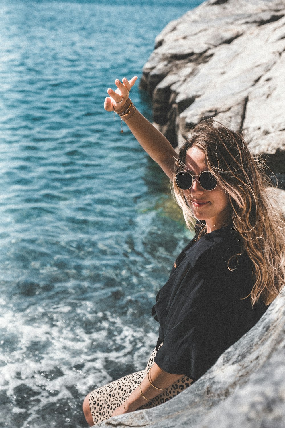 a woman sitting on top of a rock next to a body of water