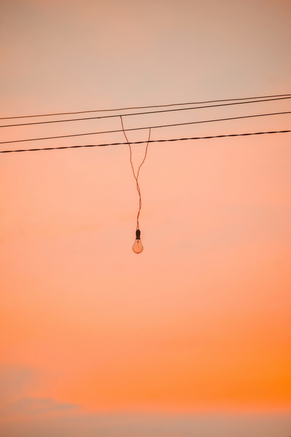 une ampoule suspendue à une ligne électrique au coucher du soleil