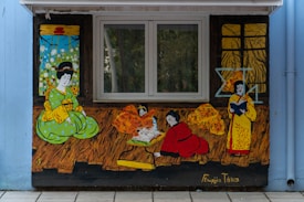 A mural featuring stylized figures in traditional Asian attire engaged in various activities. The vibrant colors and illustrative style suggest cultural or educational themes. One figure in a green outfit sits with a contemplative expression, while another in red kneels, possibly writing or reading from a scroll. A third figure in yellow holds a book. Decorative backdrops of windows and patterns add depth to the scene.