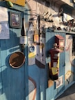 A wall filled with eclectic decorations including various clocks, frames, a red postbox, and eclectic artwork. The setting conveys a whimsical, artistic vibe with mixed media and unique objects fixed on textured walls under warm lighting.
