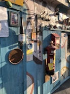 A wall filled with eclectic decorations including various clocks, frames, a red postbox, and eclectic artwork. The setting conveys a whimsical, artistic vibe with mixed media and unique objects fixed on textured walls under warm lighting.