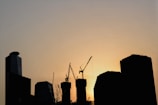 A city skyline with ongoing construction and cranes at sunset.