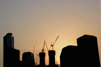 Dubai skyline at sunset with cranes and active construction sites in the foreground.