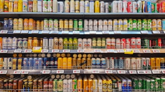 A supermarket aisle showcasing an extensive variety of canned beverages on multiple shelves. Different brands, designs, and sizes of cans are neatly organized, creating a colorful and visually appealing display.