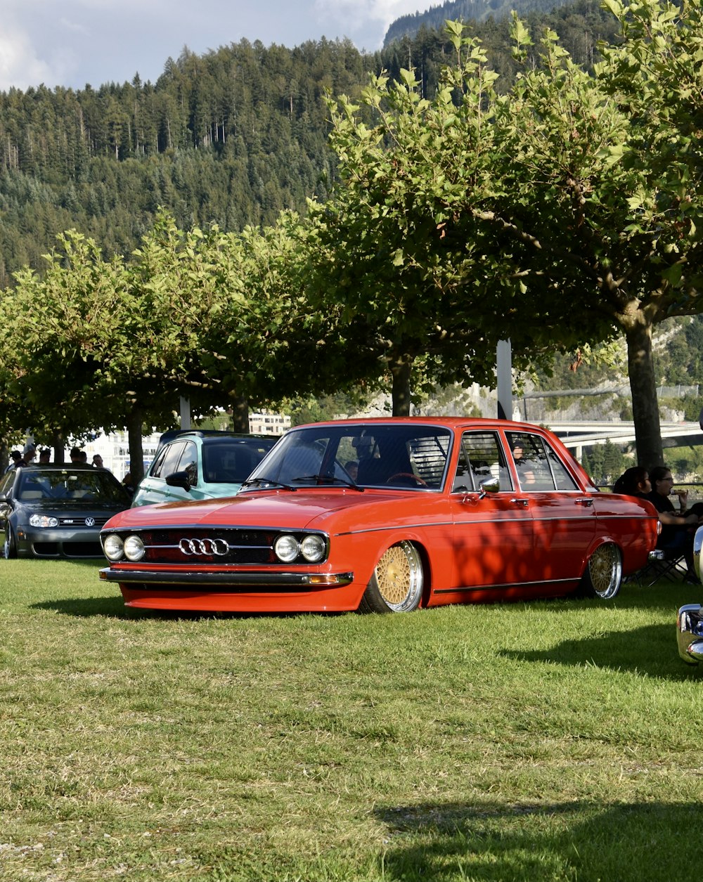 a red car parked in the grass next to trees