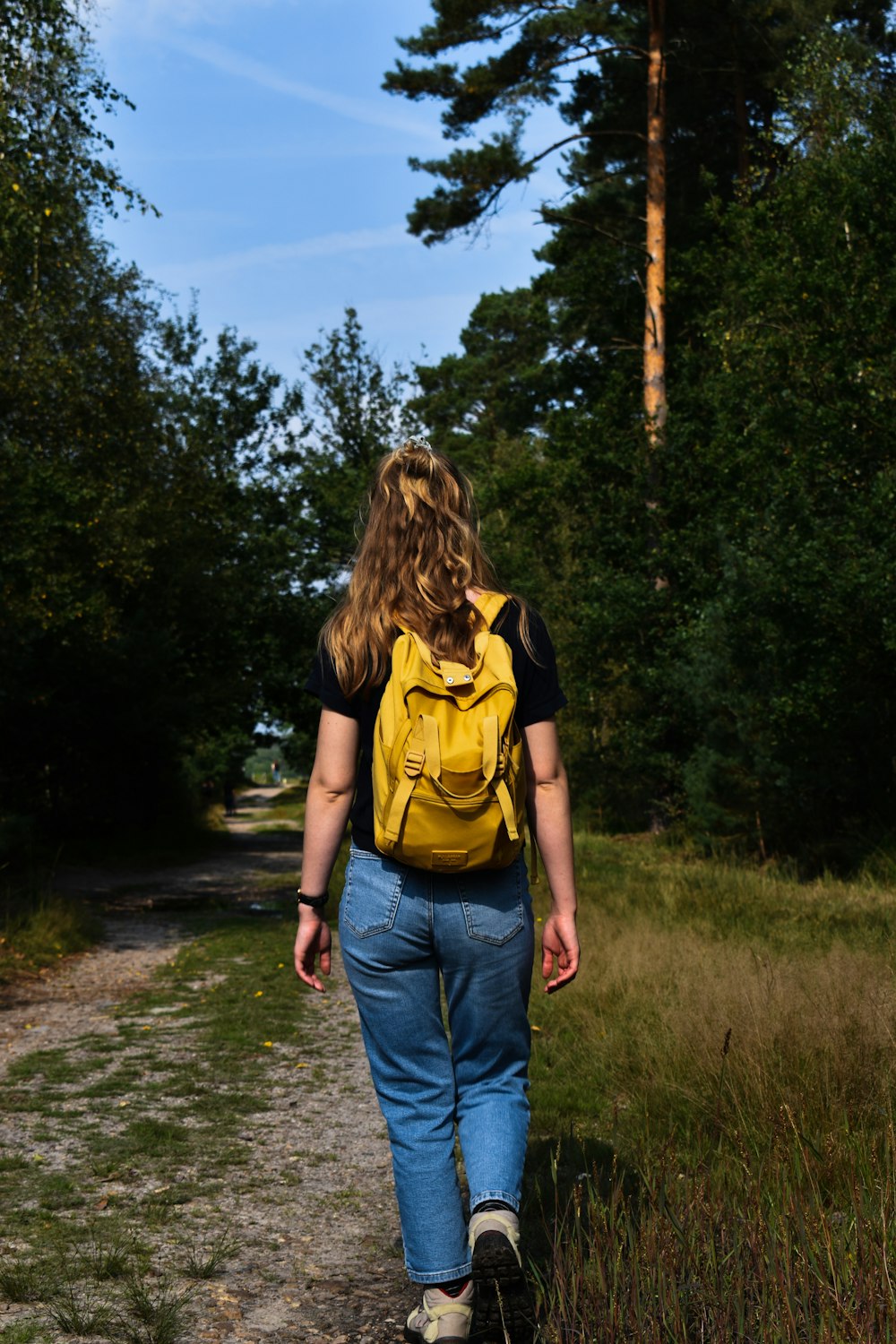 a woman with a yellow backpack walking down a path