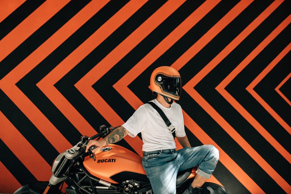 a man sitting on a motorcycle in front of a black and orange wall