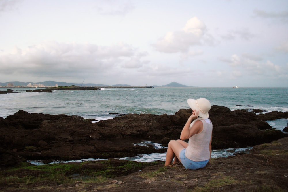 a woman sitting on a rock near the ocean