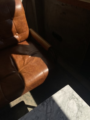 A classic leather armchair with rich brown tones, placed beside a wooden side table with a vintage lamp.