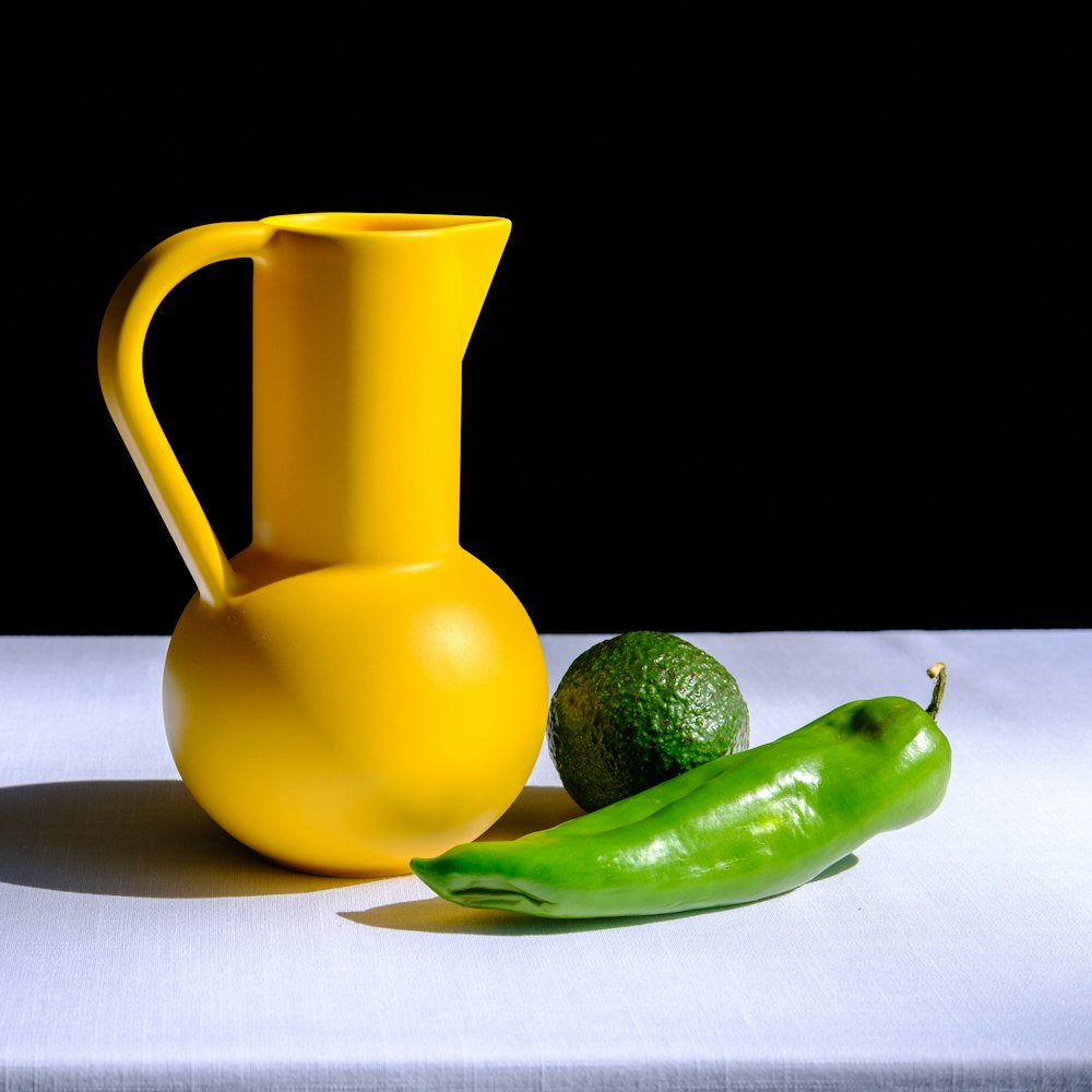 a yellow vase sitting next to a green pepper