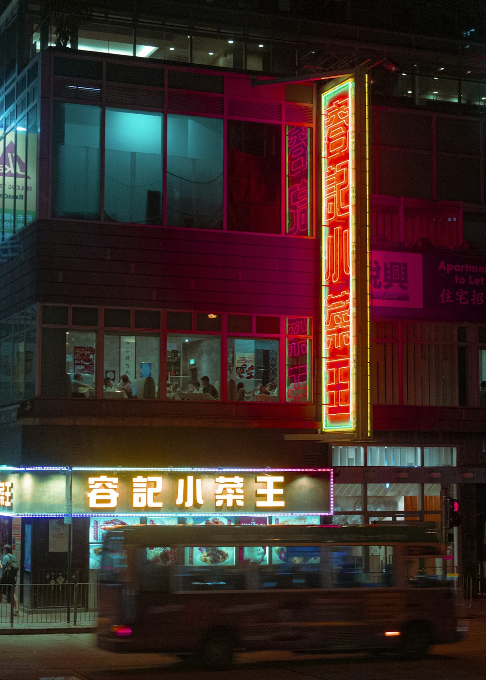 a bus driving past a tall building at night