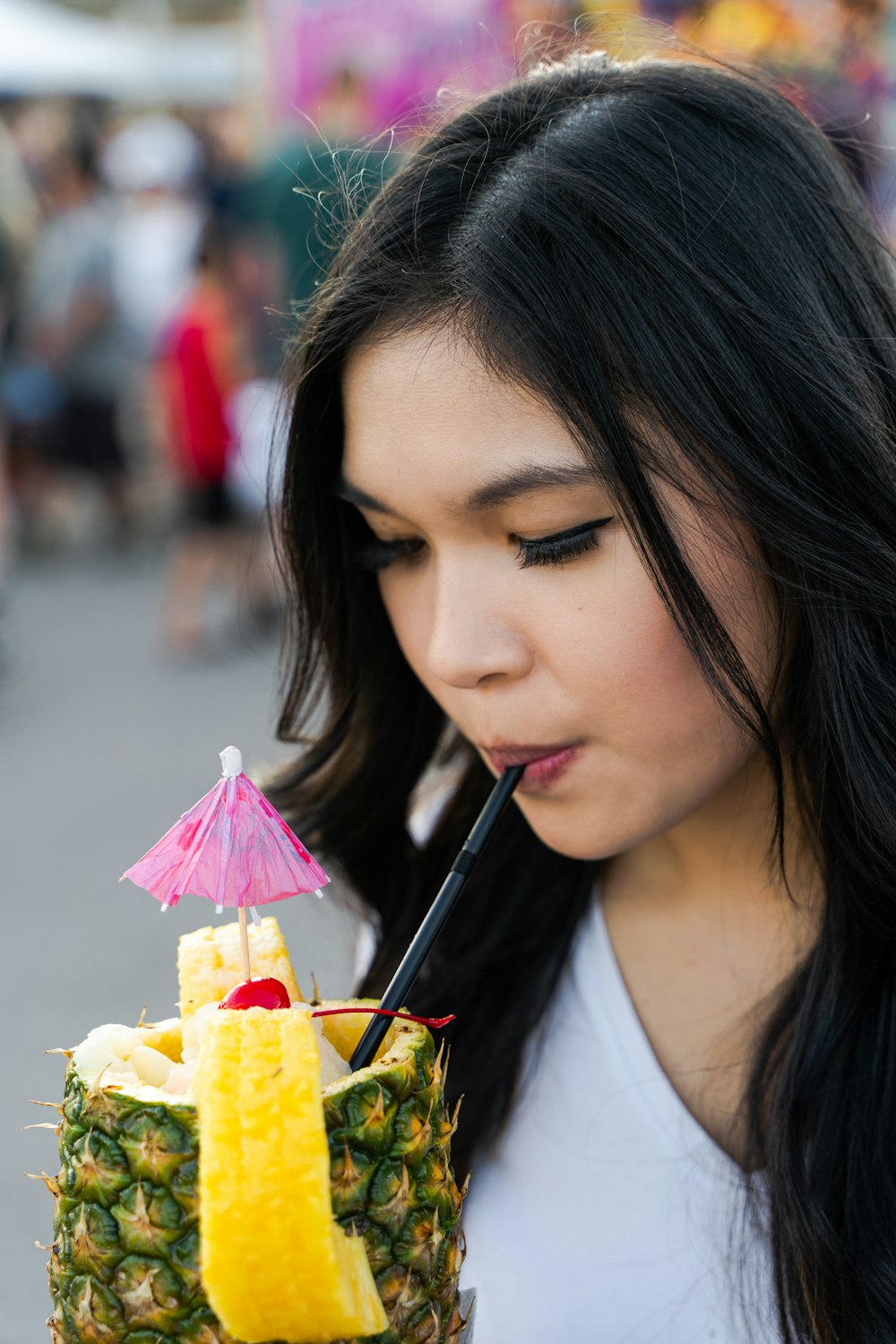 a woman holding a pineapple with a straw in her mouth