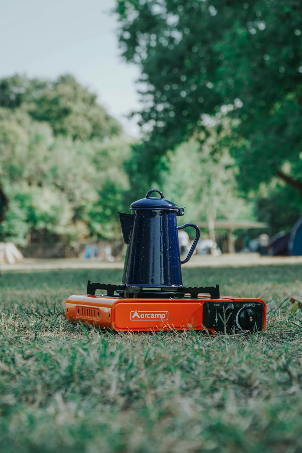 an orange and black coffee pot sitting on top of a lawn