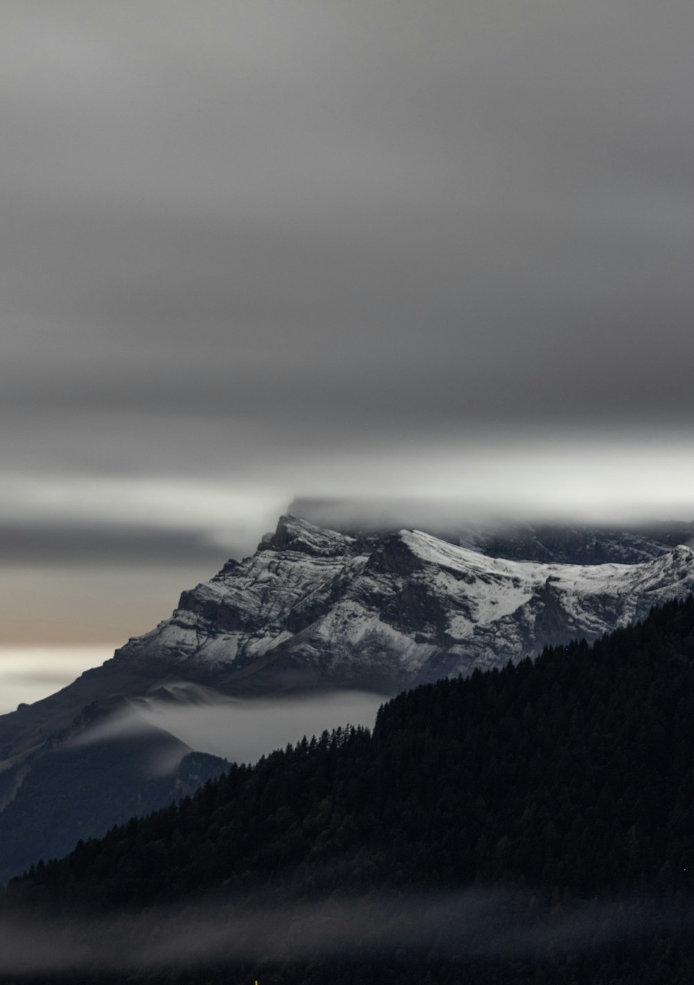 a mountain covered in snow and clouds under a cloudy sky