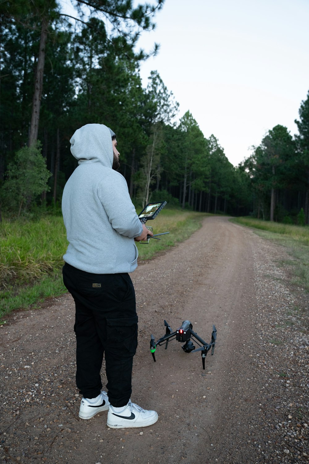 a man standing on a dirt road holding a remote control helicopter