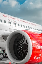 A close-up view of the engine of an airplane with a red casing and white body. The airplane has windows along the body and the text 'The airline of the Maltese Islands' written on its side.