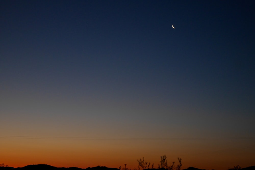 the moon is setting in the sky over the mountains