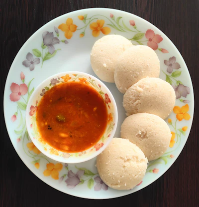 Steaming hot idlis served with coconut chutney and sambar in a traditional plate.