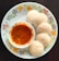 A close-up of a steaming plate of fluffy idlis with coconut chutney and sambar.