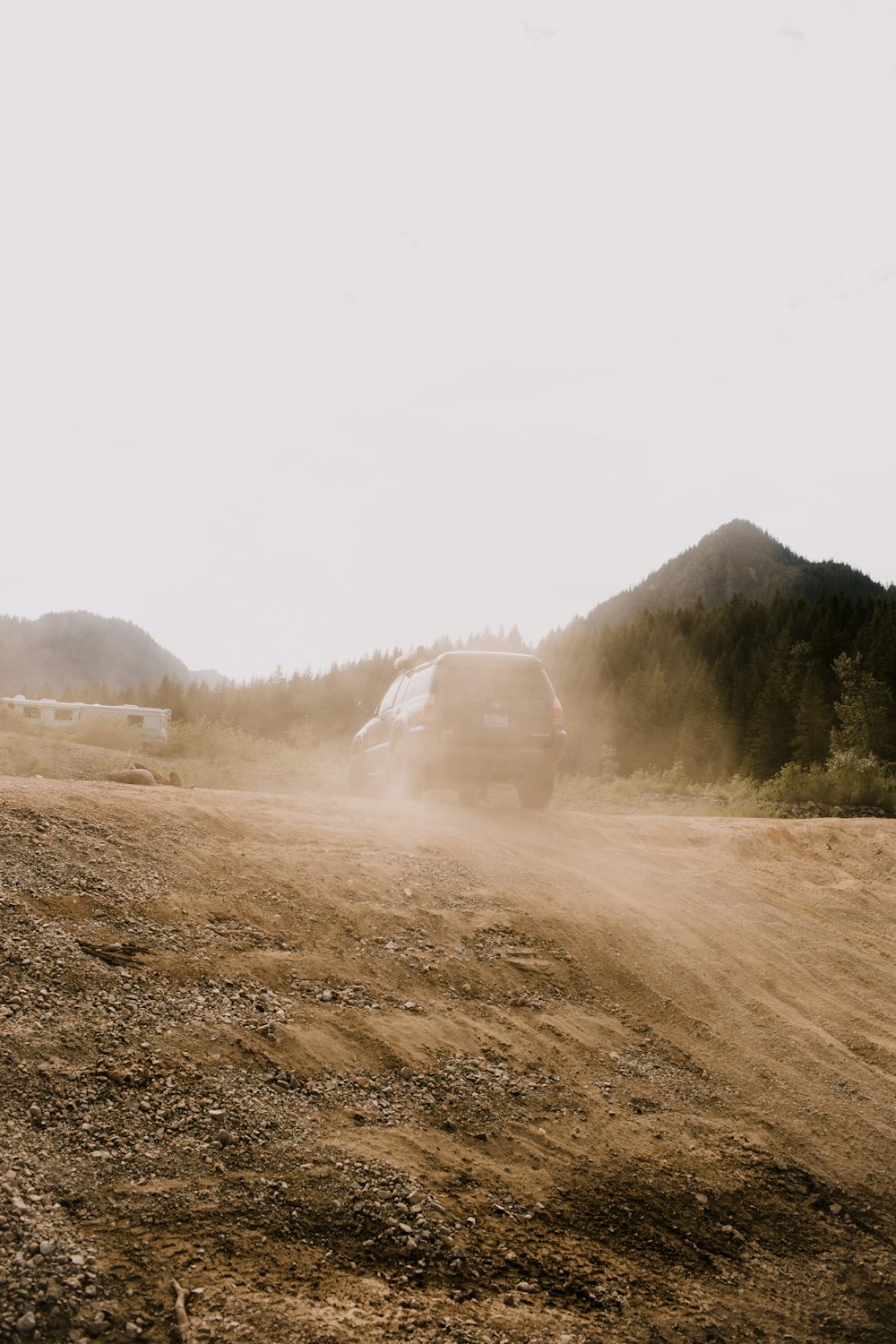 a truck driving down a dirt road near a forest