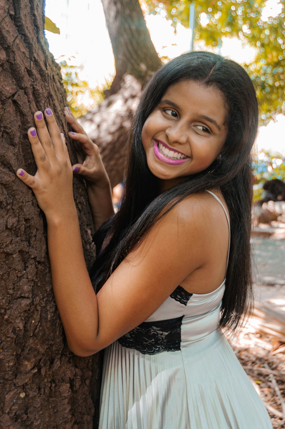 a girl in a white dress leans against a tree