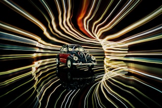 A classic, vintage car model is positioned against a backdrop of dynamic, swirling light trails. The lights create a sense of motion and energy, contrasting with the stationary car. The reflective surface beneath the car enhances the illusion of depth and movement.
