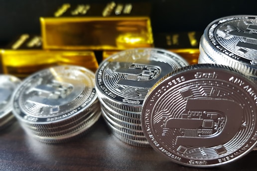 Stack of certified gold bars and silver coins with a market price chart in the background.