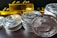 A stack of silver-colored cryptocurrency coins is prominently displayed in front of several shiny gold bars. The coins feature intricate engraving and digital circuit designs.