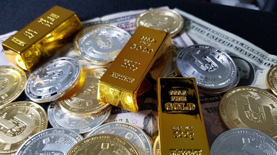 Several gold bars are placed on top of a pile of bitcoin coins and US dollar bills, indicating a scene of wealth and finance.
